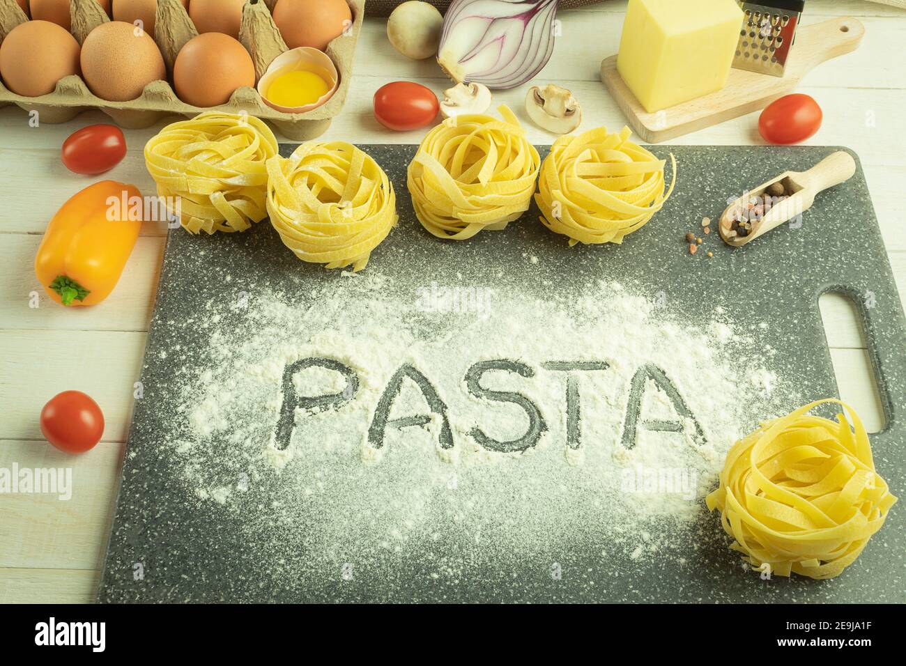 Das Wort Pasta wird mit dem Finger auf das Mehl geschrieben. Hausgemachte Eiernudeln auf dem Tisch als Hintergrund mit Platz für Text. Makkaroni mit Tomaten Stockfoto