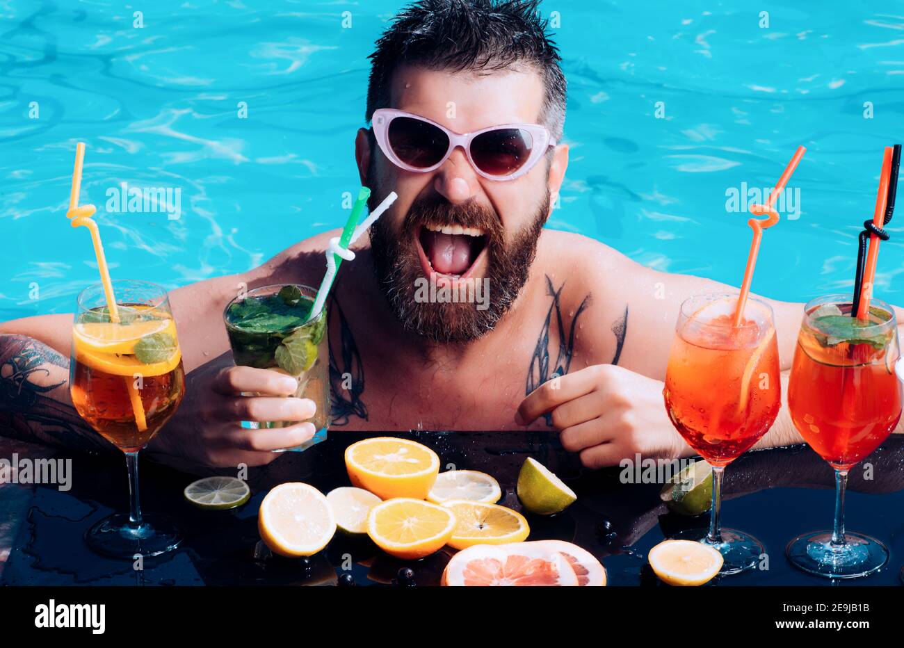 Poolparty. Mann schwimmend und Alkohol trinken. Urlaub Miami oder Malediven im Sommer. Cocktail mit Obst beim bärtigen Mann im Pool. Stockfoto