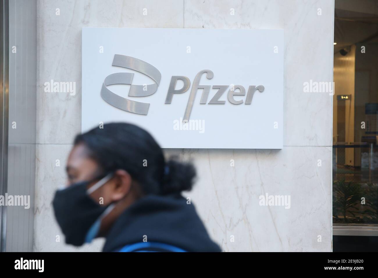 New York City, NY USA der Mann mit einer Maske geht am Schild für den Pfizer World Headquarters in der 42nd Street in Manhattan vorbei Stockfoto