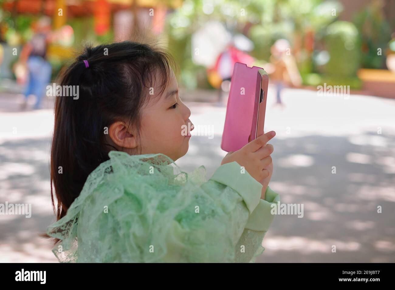 Ein nettes junges asiatisches Mädchen hält ein rosa Smartphone und versucht, ein Bild in ihrem Urlaub zu machen. Stockfoto