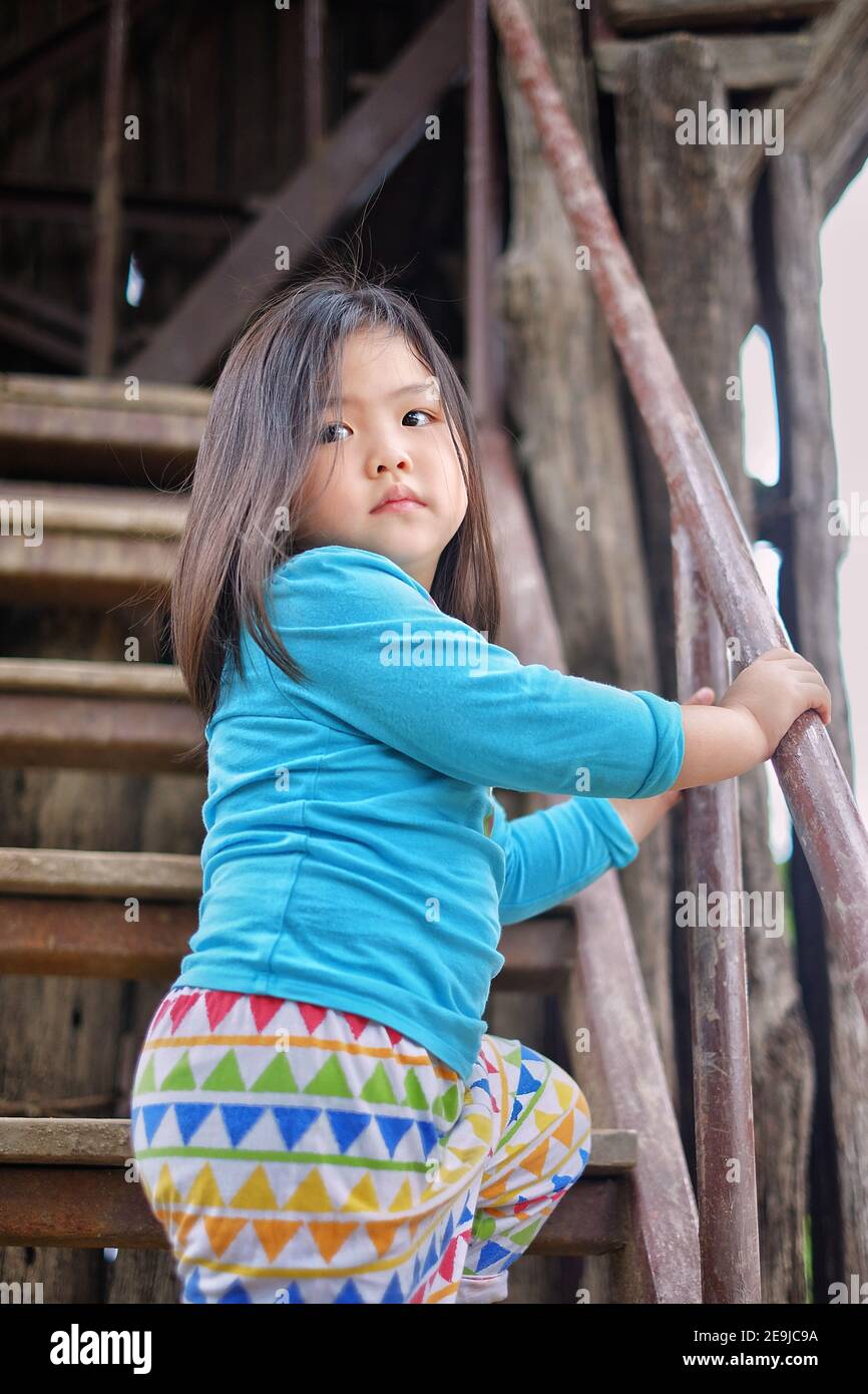 Ein süßes junges asiatisches Mädchen spielt auf einem Spielplatz und klettert eine Treppe hinauf zu einer Rutsche darüber. Stockfoto