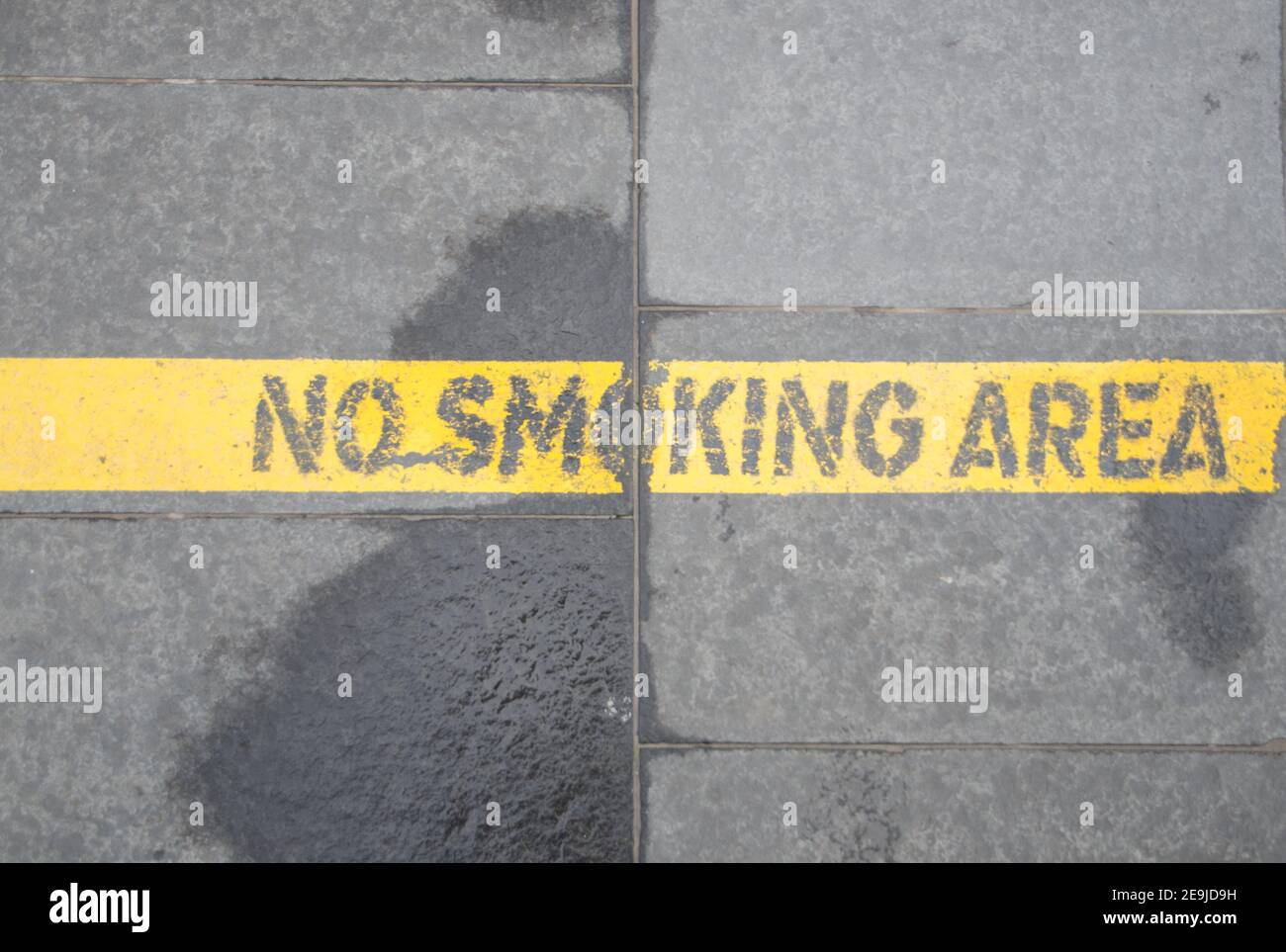 Rauchen ist nach dieser Linie verboten. Eine gelbe Linie auf dem Asphalt begrenzt den Nichtraucherbereich auf dem Platz eines Geschäfts- und Geschäftsviertels Stockfoto