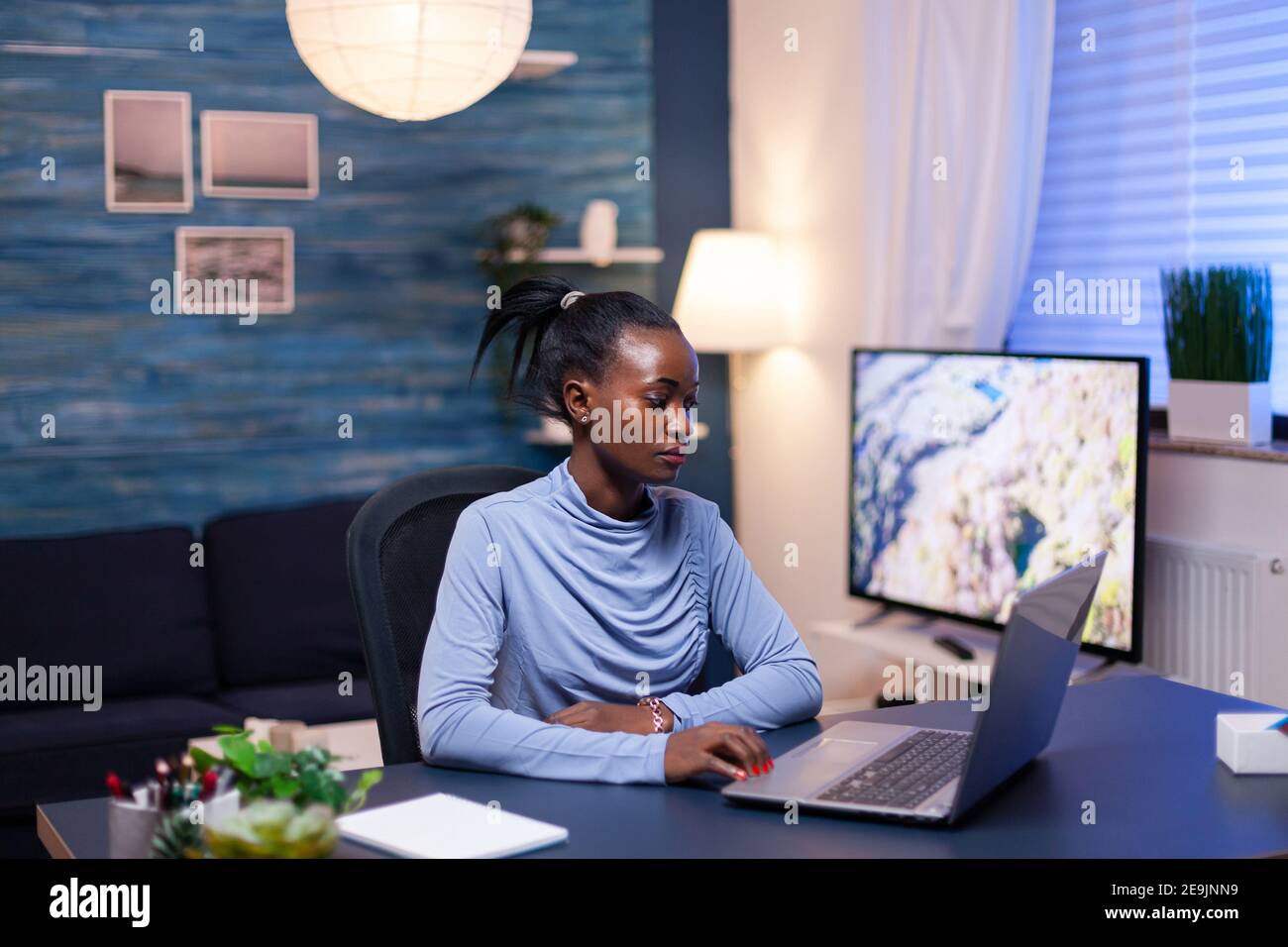 Dunkelhäutiger Freiberufler, der spät in der Nacht Dokumentation auf einem Laptop-Computer im Wohnzimmer liest. Schwarzer Unternehmer sitzt in persönlichen Arbeitsplatz Schreiben auf der Tastatur. Stockfoto