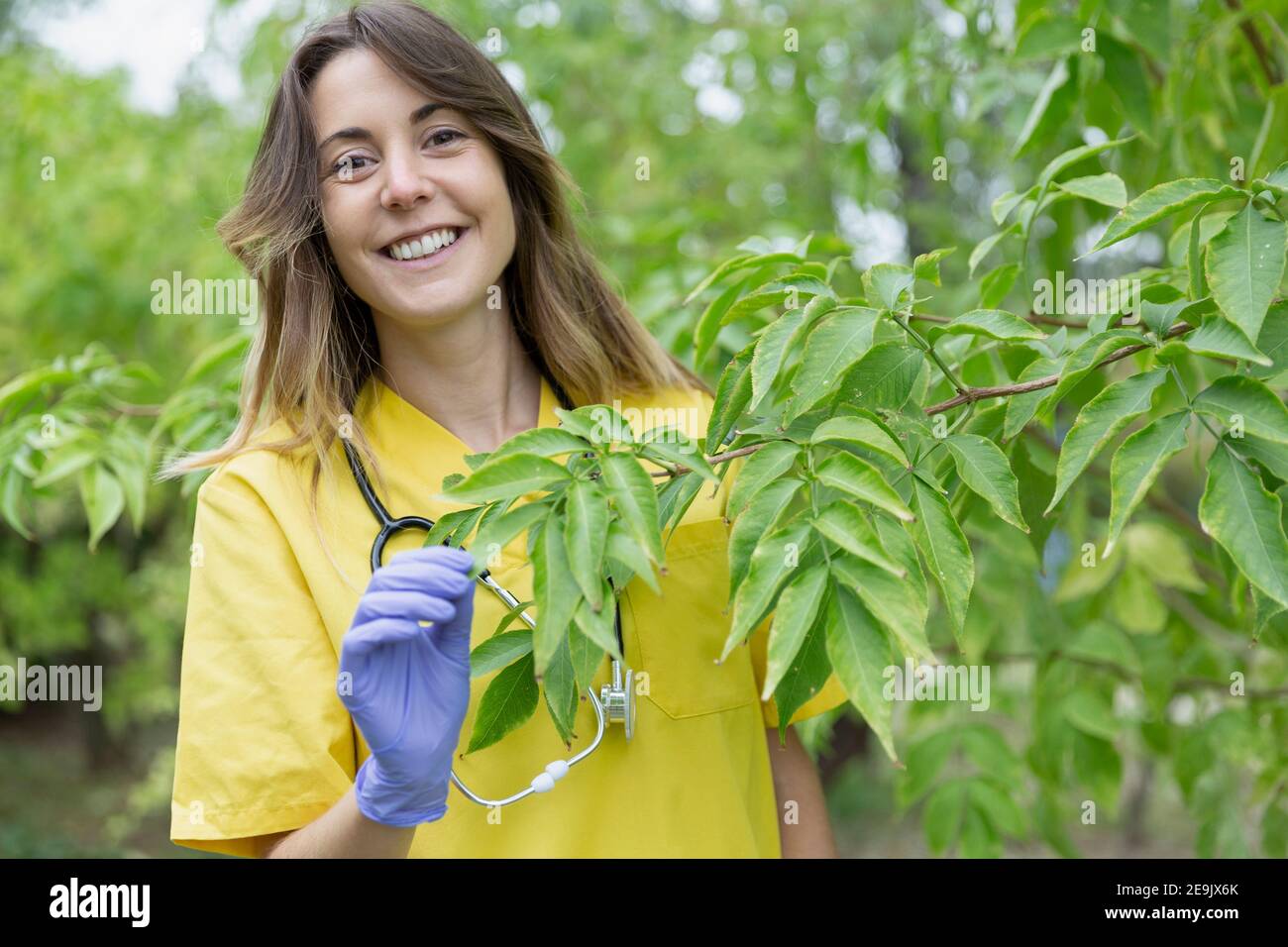 Porträt einer jungen lächelnden Krankenschwester Frau, die sich um Pflanzen in der Natur kümmert. Leerzeichen für Text. Stockfoto