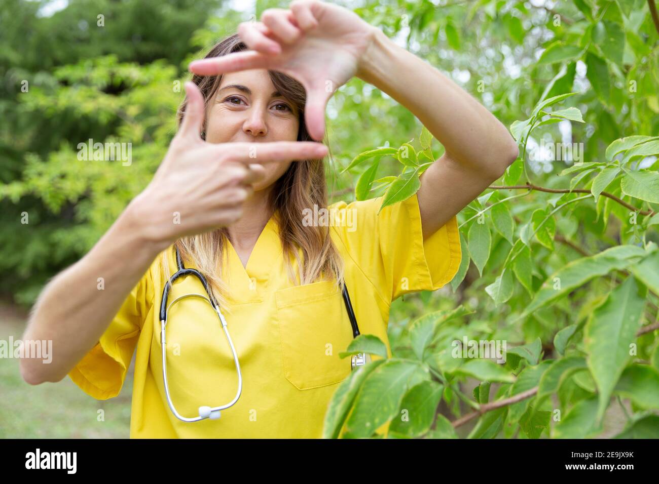 Eine junge Krankenschwester umrahmt ihr Gesicht mit ihren Händen als Selbstporträt. Sie ist in der Natur. Leerzeichen für Text. Stockfoto