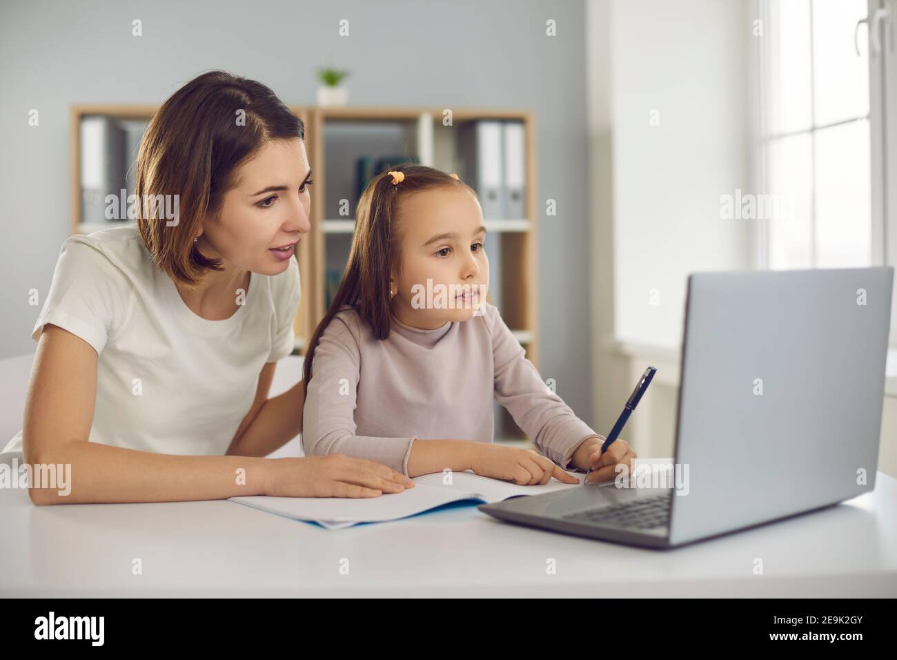 Mutter und kleines Mädchen Tochter sitzen zusammen und machen Hausaufgaben Oder Aufgaben während des Online-Unterrichts Stockfoto