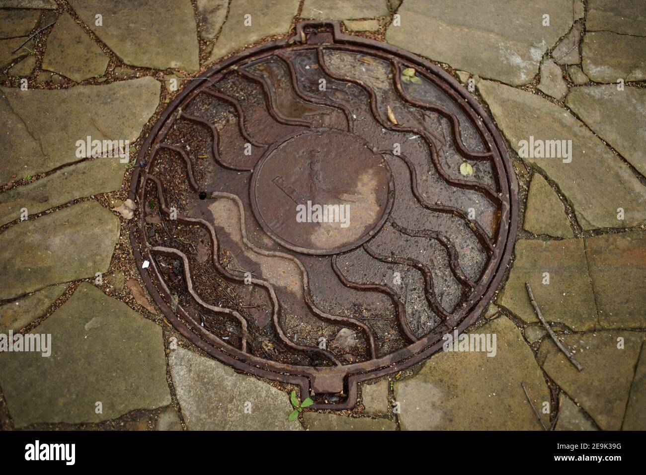 Altes Mannloch mit Buchstabe k nass nach Regen. Stockfoto
