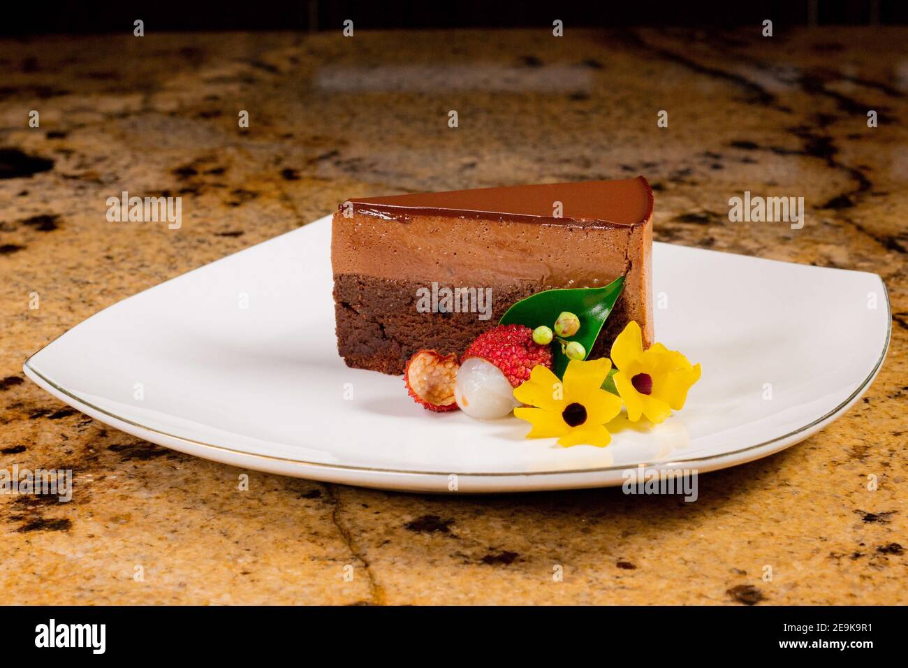 Ein Stück Schokoladenkuchen und Mousse mit gelben Blumen, Litschi auf einem weißen Teller. Stockfoto