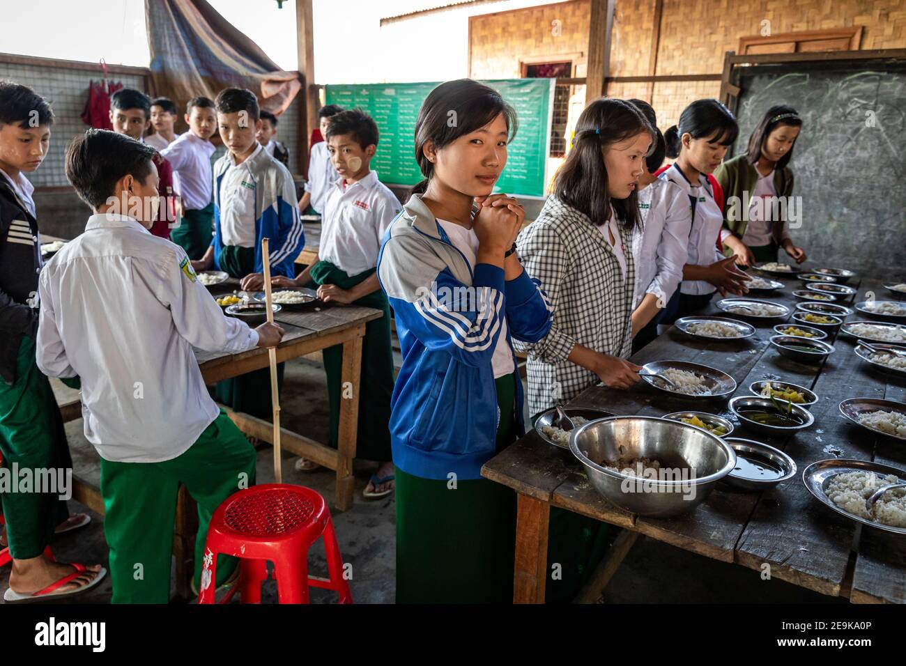 Die Schüler, von denen die meisten Waisenkinder sind, die aus dem Bürgerkrieg geflohen sind, kommen während ihrer Mittagspause in ihr Chinpwi Education Internat in Myikyina, Myanmar. Die Direktorin, Mai WGI Drehhe, verteilt das Essen aus den großen Kochtöpfen. Stockfoto