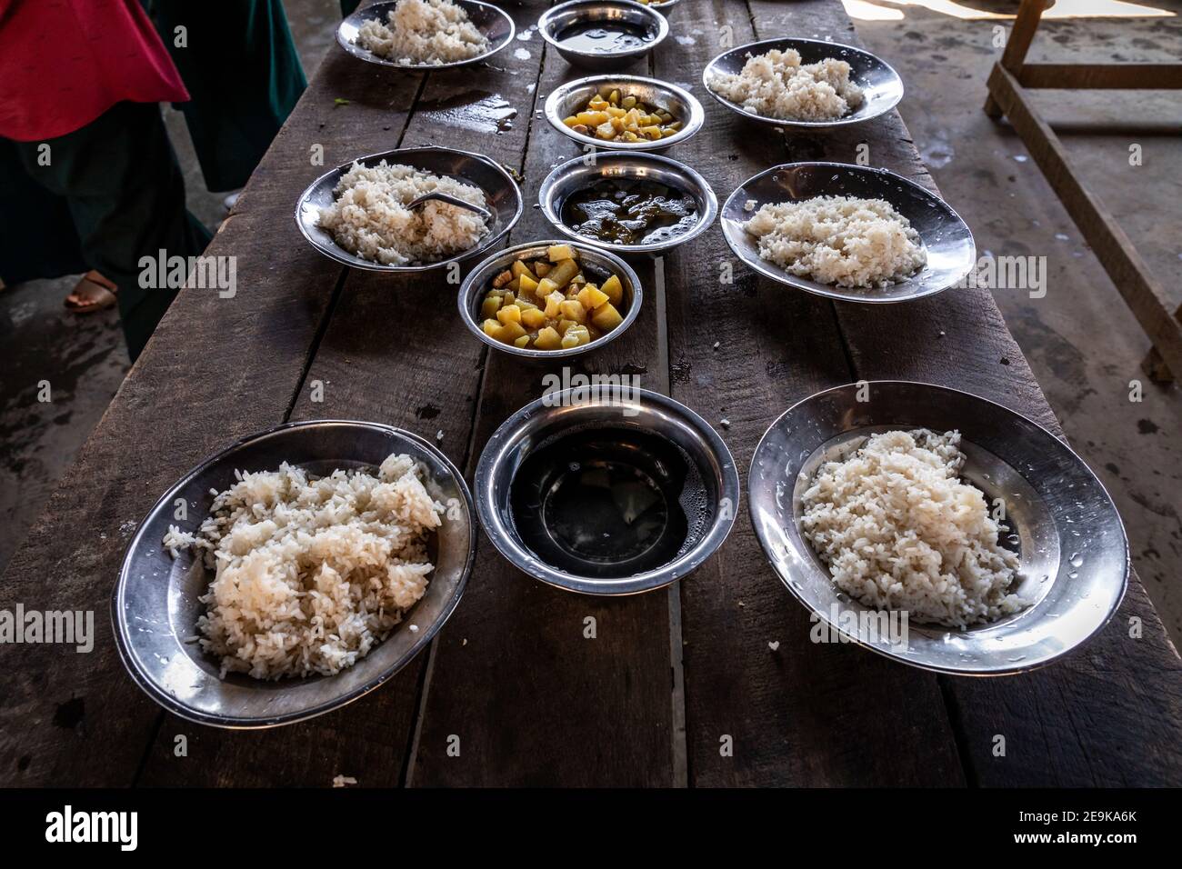 Die Schüler, von denen die meisten Waisenkinder sind, die aus dem Bürgerkrieg geflohen sind, kommen während ihrer Mittagspause in ihr Chinpwi Education Internat in Myikyina, Myanmar. Die Direktorin, Mai WGI Drehhe, verteilt das Essen aus den großen Kochtöpfen. Stockfoto