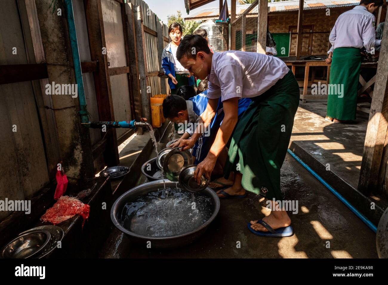 Die Schüler, von denen die meisten Waisenkinder sind, die aus dem Bürgerkrieg geflohen sind, kommen während ihrer Mittagspause in ihr Chinpwi Education Internat in Myikyina, Myanmar. Die Direktorin, Mai WGI Drehhe, verteilt das Essen aus den großen Kochtöpfen. Stockfoto