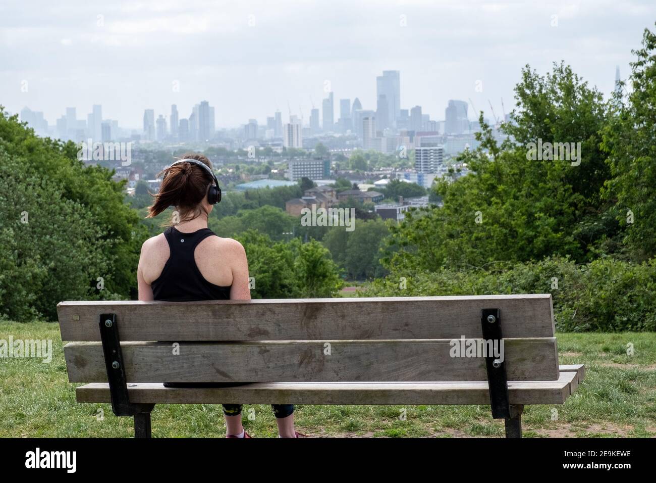 Eine junge Frau in sportlicher Kleidung sitzt auf einer Bank Vom Parliament Hill aus blickt man auf die Skyline von London Aussichtspunkt auf Hamstead Heath Stockfoto