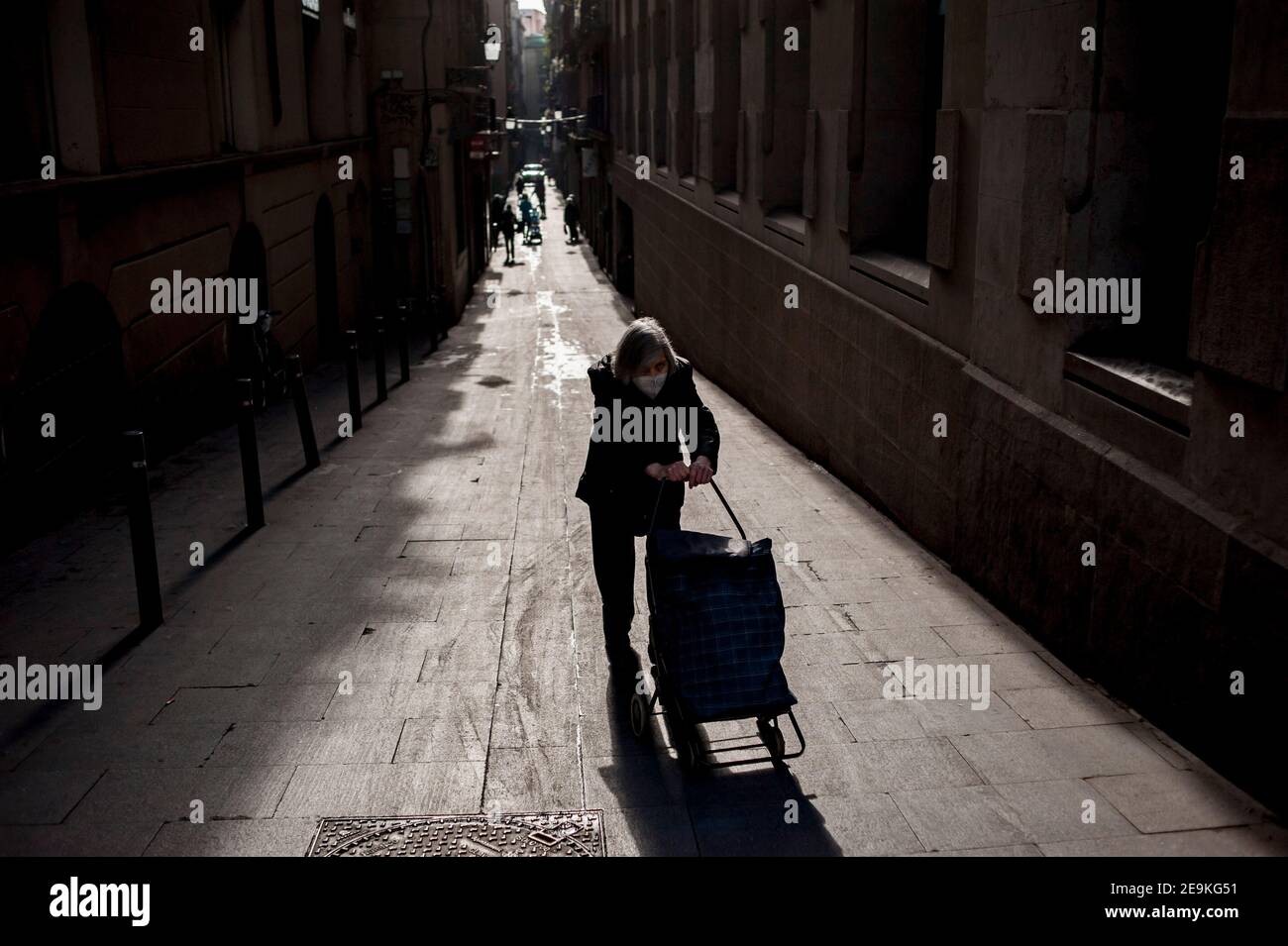 Eine Frau mit Gesichtsmaske schiebt den Einkaufswagen an einem Hang im Gotischen Viertel von Barcelona hoch. Die Zahl der Todesopfer in Spanien durch das Coronavirus beträgt heute 60.802. Stockfoto