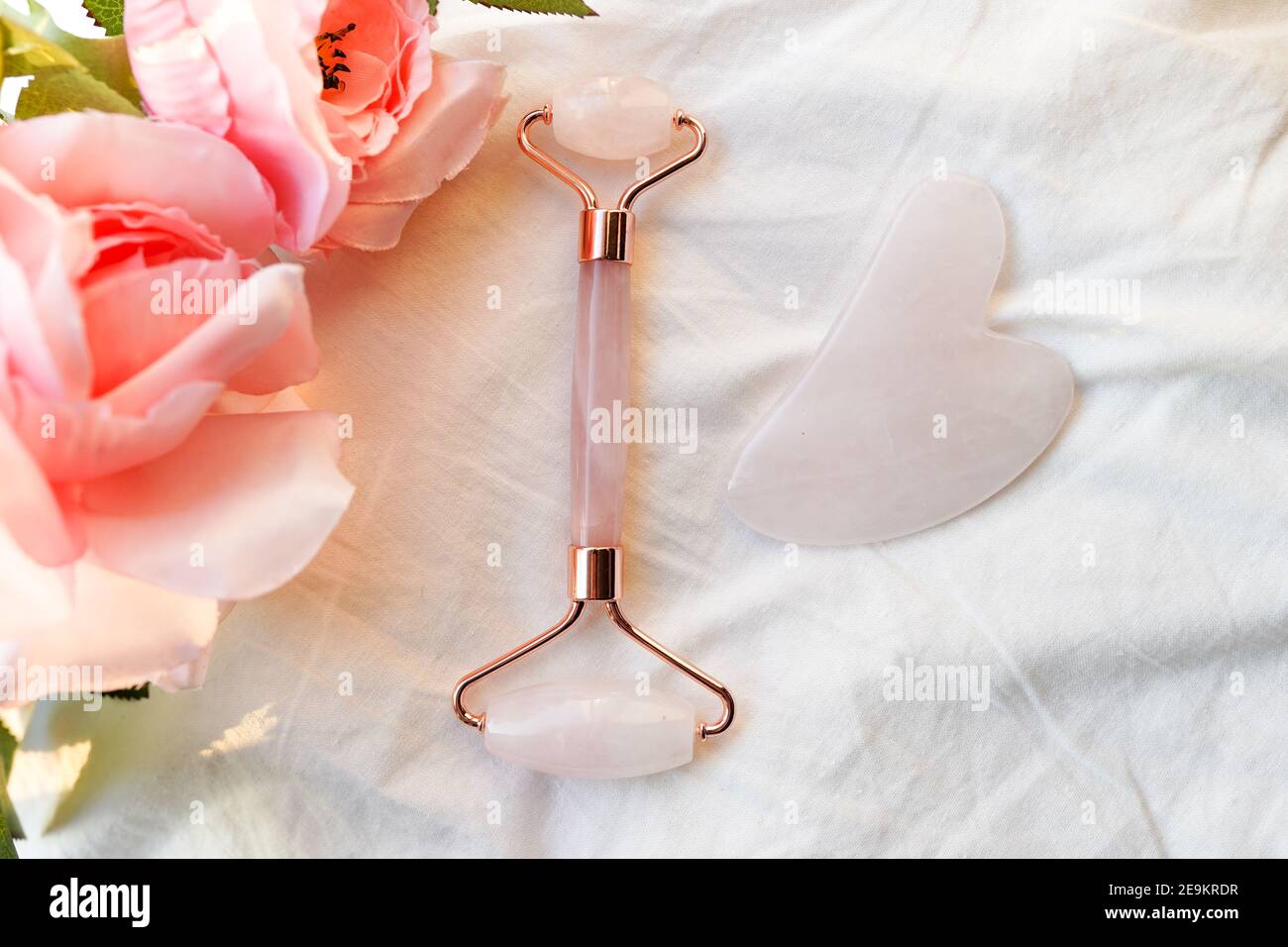 Pink Face Roller und Gua Sha Massagegerät aus natürlichen Jade nephritis Stein und Blumen stieg auf weißem Hintergrund. Konzept der Gesichtsmassage. Stockfoto