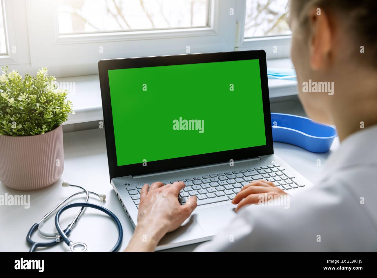 Weibliche Arzt Eingabe auf ihrem Laptop-Computer in der medizinischen Klinik Büro. Leere grünen Bildschirm mockup Stockfoto
