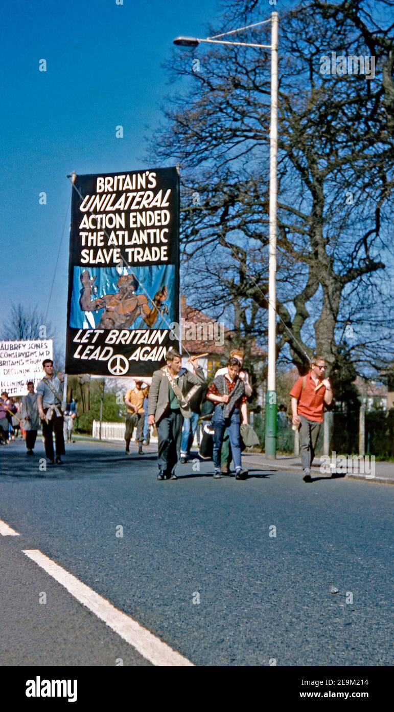 Marschers in West London, auf dem Weg nach Central London auf dem CND Aldermaston märz 1962. Sichtbar ist das markante schwarz-weiße, runde Logo, das 1958 für die britische Abrüstungsbewegung entworfen wurde – heute weithin als ‘Friedenszeichen’ angesehen. Hier bezieht sich ein riesiges Banner auf die Kampagne der CND auf die Bemühungen, den britischen Sklavenhandel zu beenden. Die Abbildung zeigt einen schwarzen Sklaven in Ketten. Stockfoto