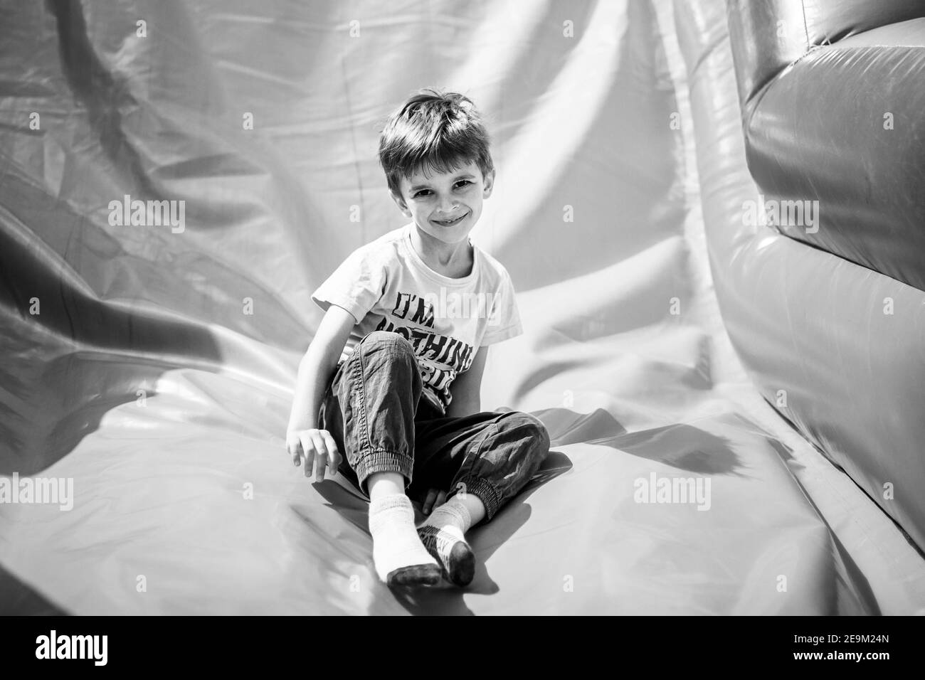 Lächelnder kleiner Junge, der auf einer aufblasbaren Rutsche spielt und die Kamera anschaut Stockfoto