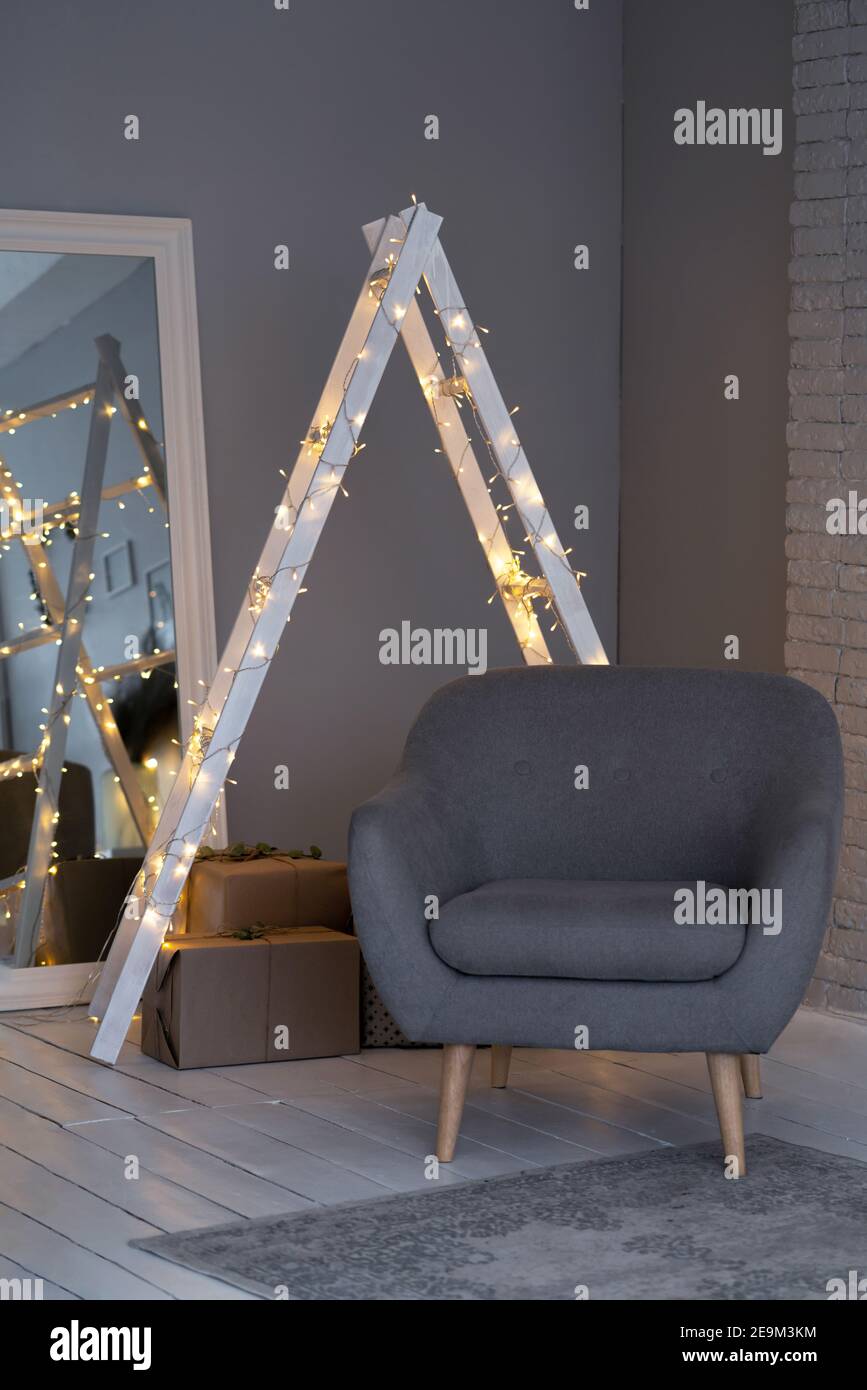 Details eines skandinavischen gemütlichen Innenraums in warmem hellbeige. Ein Sessel, ein Kissen in einem seidenen Kissenbezug, eine Leiter in den Lichtern, ein Spiegel. Stockfoto