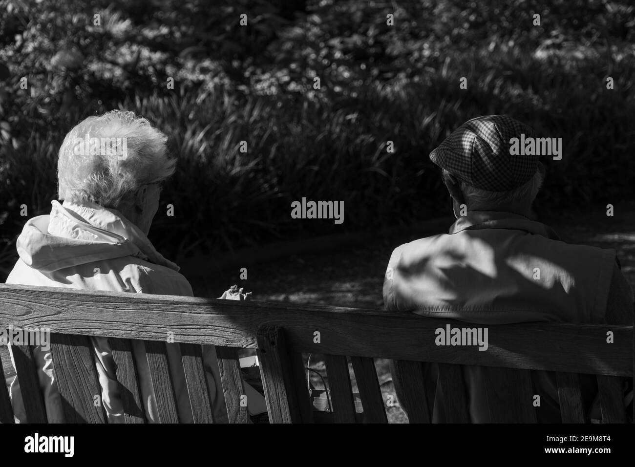Seniorenpaar, das sich auf einem hölzernen Gartenstuhl in einem schattigen Bereich in Harrogate, North Yorkshire, England, entspannen kann. Stockfoto
