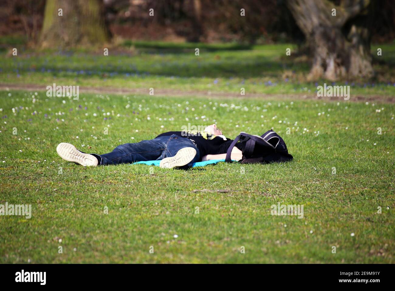 Die ersten warmen Strahlen der Frühlingssonne. Ein Mann, der sich auf einer Wiese in einem öffentlichen Park sonnt Stockfoto