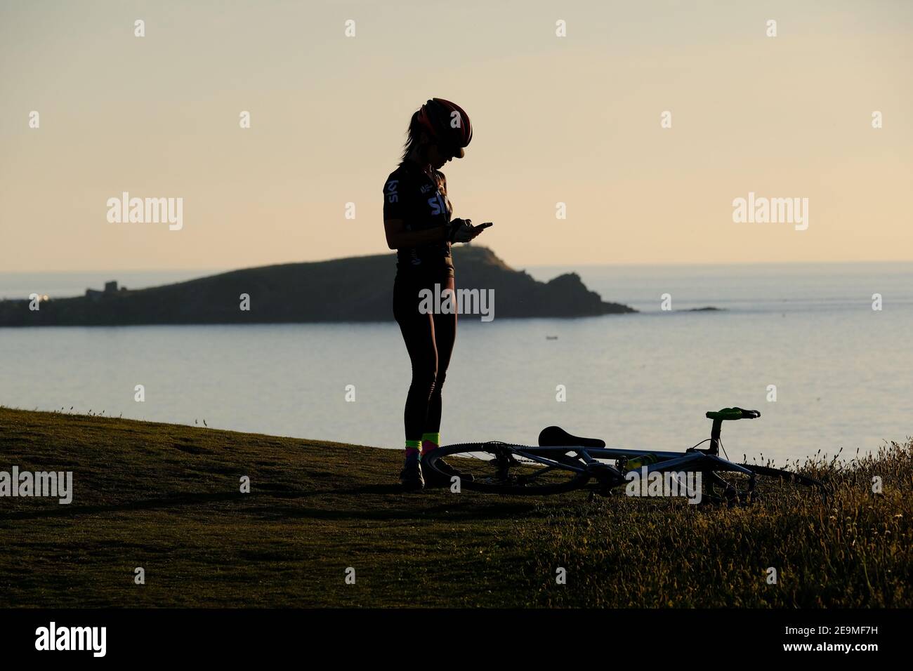Eine Radfahrerin hält an, um die Aussicht auf dem Küstenpfad in Newquay in Cornwall, Großbritannien, einzufangen. Stockfoto