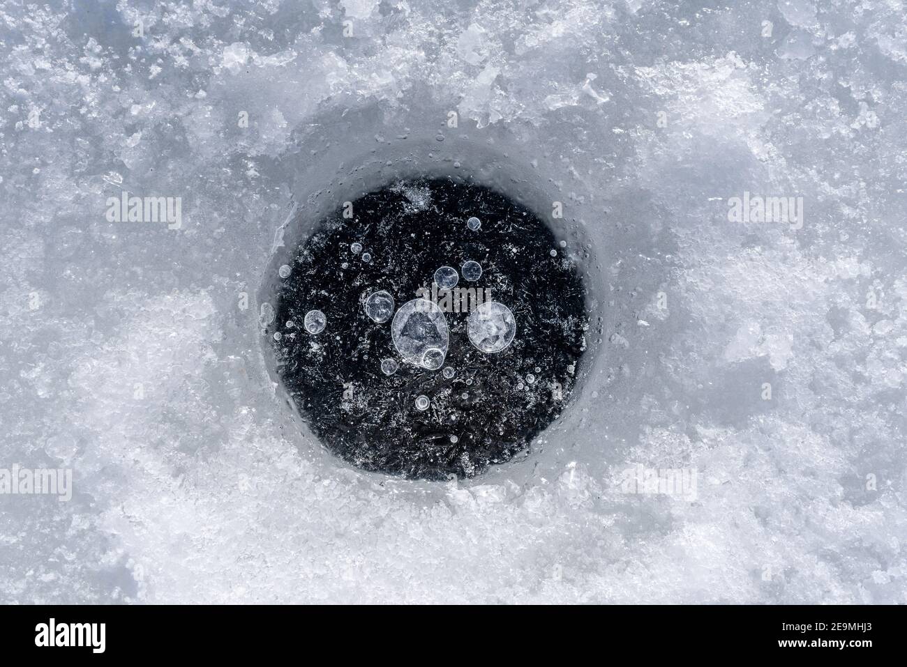 Gefrorene Wasserblasen in einem Loch im Eis auf einem See zum Angeln. Stockfoto