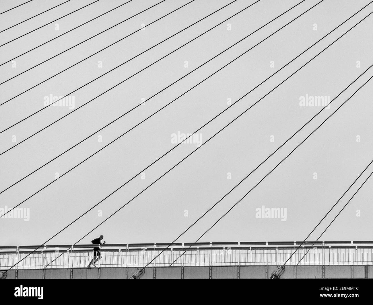 Ein Mann geht an einem sonnigen Wintertag in Fuengirola über eine Hängebrücke vor dem Meer. Stockfoto