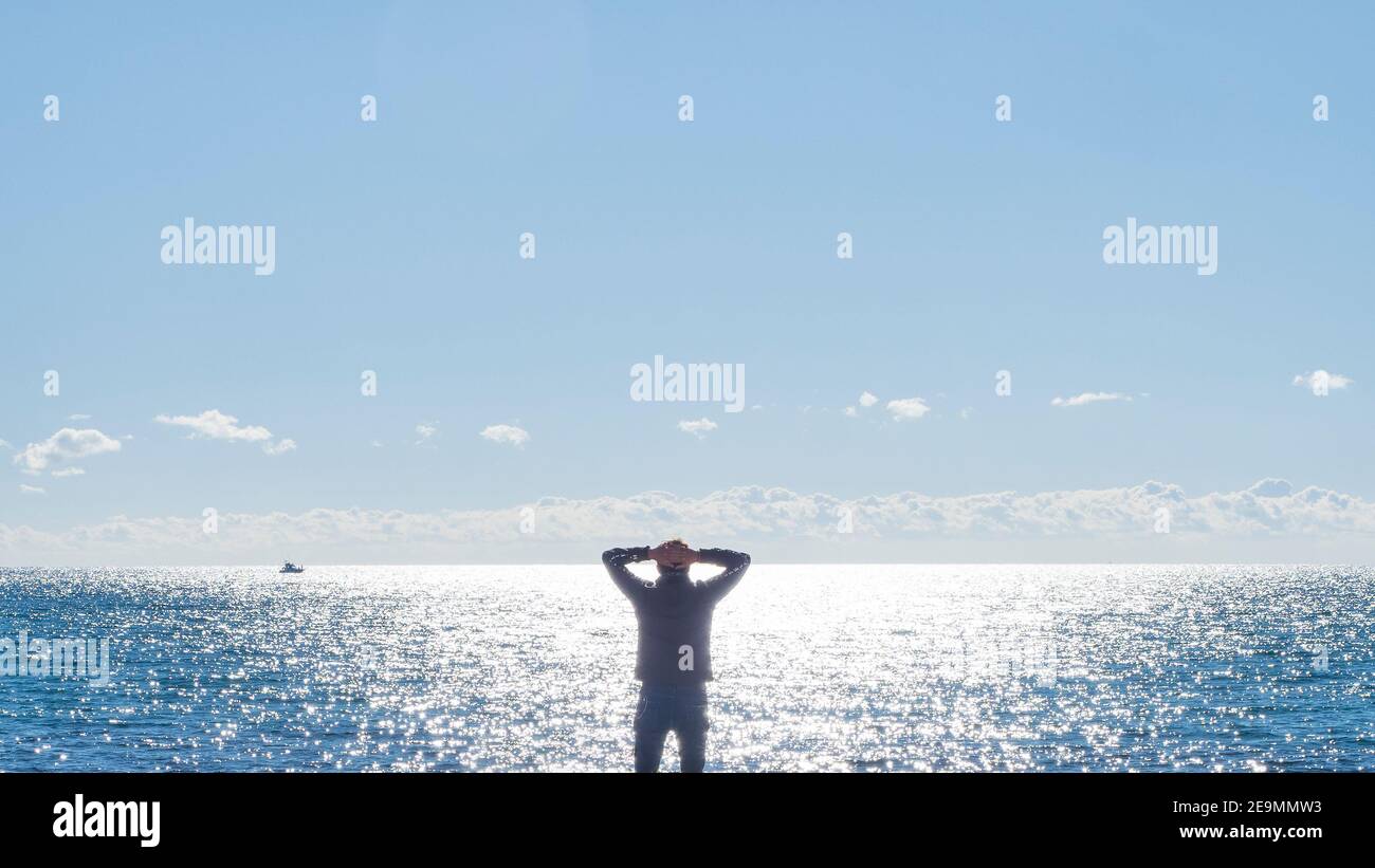 Silhouette eines Mannes mit Rücken und Armen auf dem Kopf, der vor dem Meer meditiert. Stockfoto