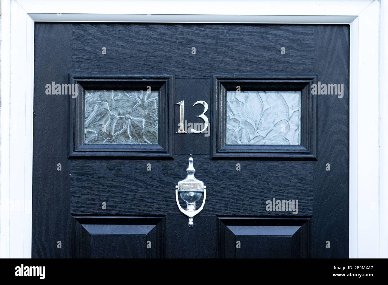 Hausnummer 13 in silberner Metallziffer auf einem schwarzen Holztür Stockfoto
