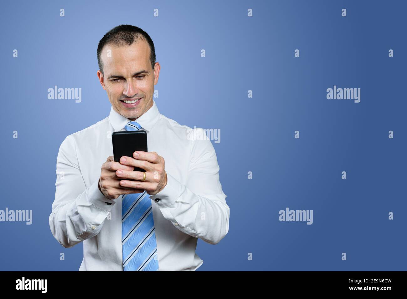 Reifer brasilianischer Mann trägt formelle Kleidung, Krawatte und Blick auf sein Smartphone. Blauer Hintergrund. Stockfoto