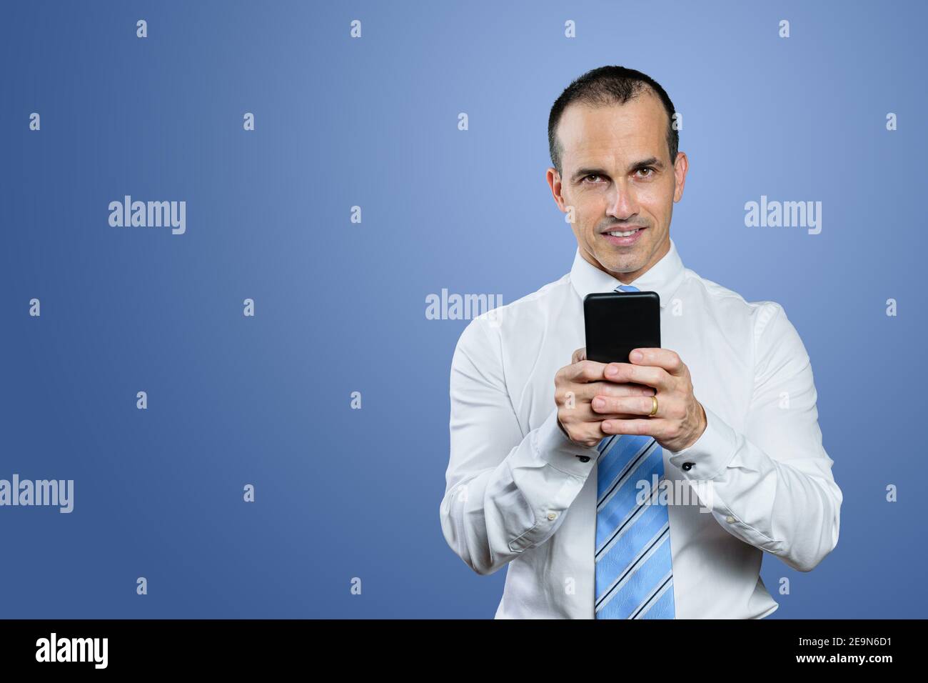 Reifer brasilianischer Mann, in formeller Kleidung, Krawatte, Smartphone halten und Kamera betrachten. Blauer Hintergrund. Stockfoto