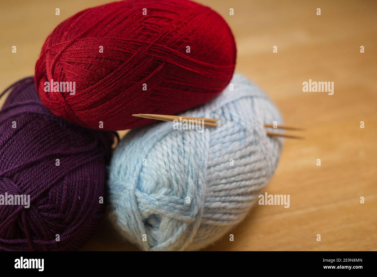 Ein lockerer Stapel von Knäueln in verschiedenen Farben des Strickgarns mit zwei kleinen Nadeln hervorstehend. Künstlerische Schärfentiefe Hintergrund von Holztisch. Stockfoto