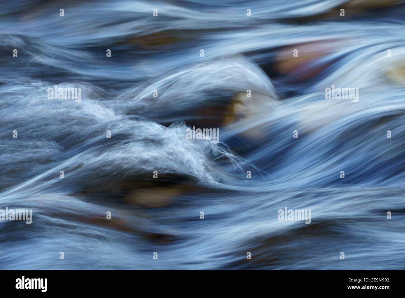 Nahaufnahme von bewegungsunscharfen Wasserschnellen, die über einem Steinkobbel fließen Flussbett Stockfoto