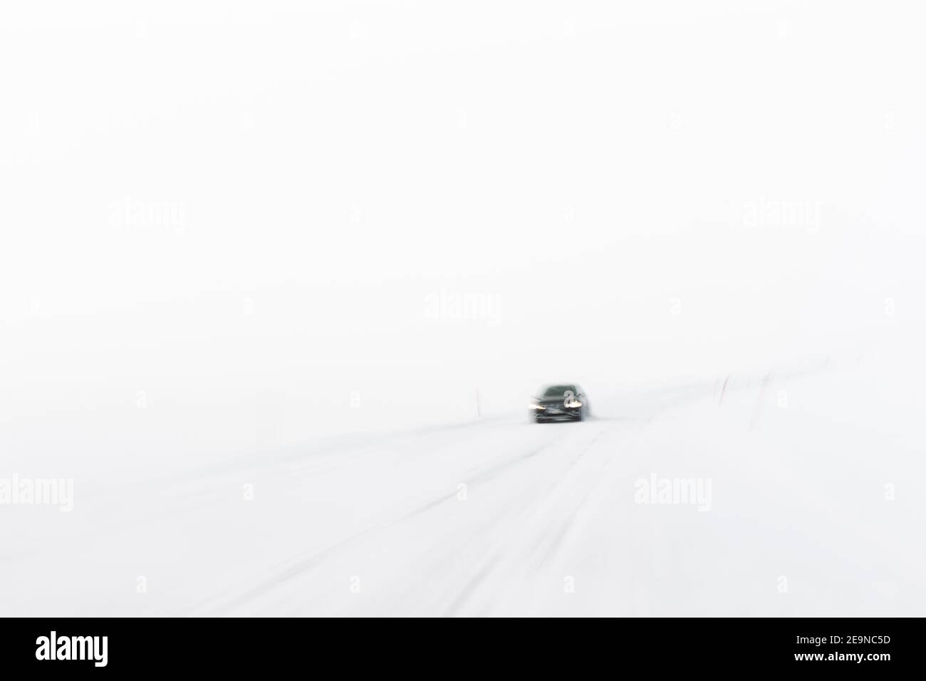 Blick auf ein Einzelauto, das während eines Schneesturms auf einer Schneesturm-geführten Straße entlang fährt, mit einem Slow-Shutter zur enthüllenden Bewegung, Norwegen Stockfoto