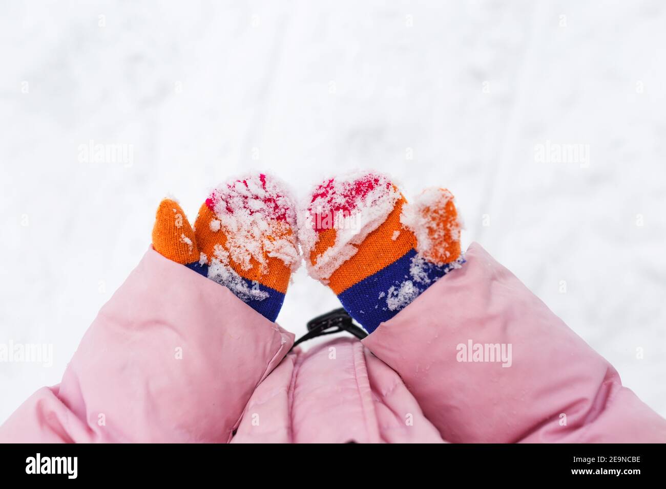 Schnee auf Fäustlingen oder Handschuhen. Kinderhände halten Hände im Schnee. Bunte gestrickte Winterhandschuhe, mit Schnee befleckt. Winterurlaub. Stockfoto