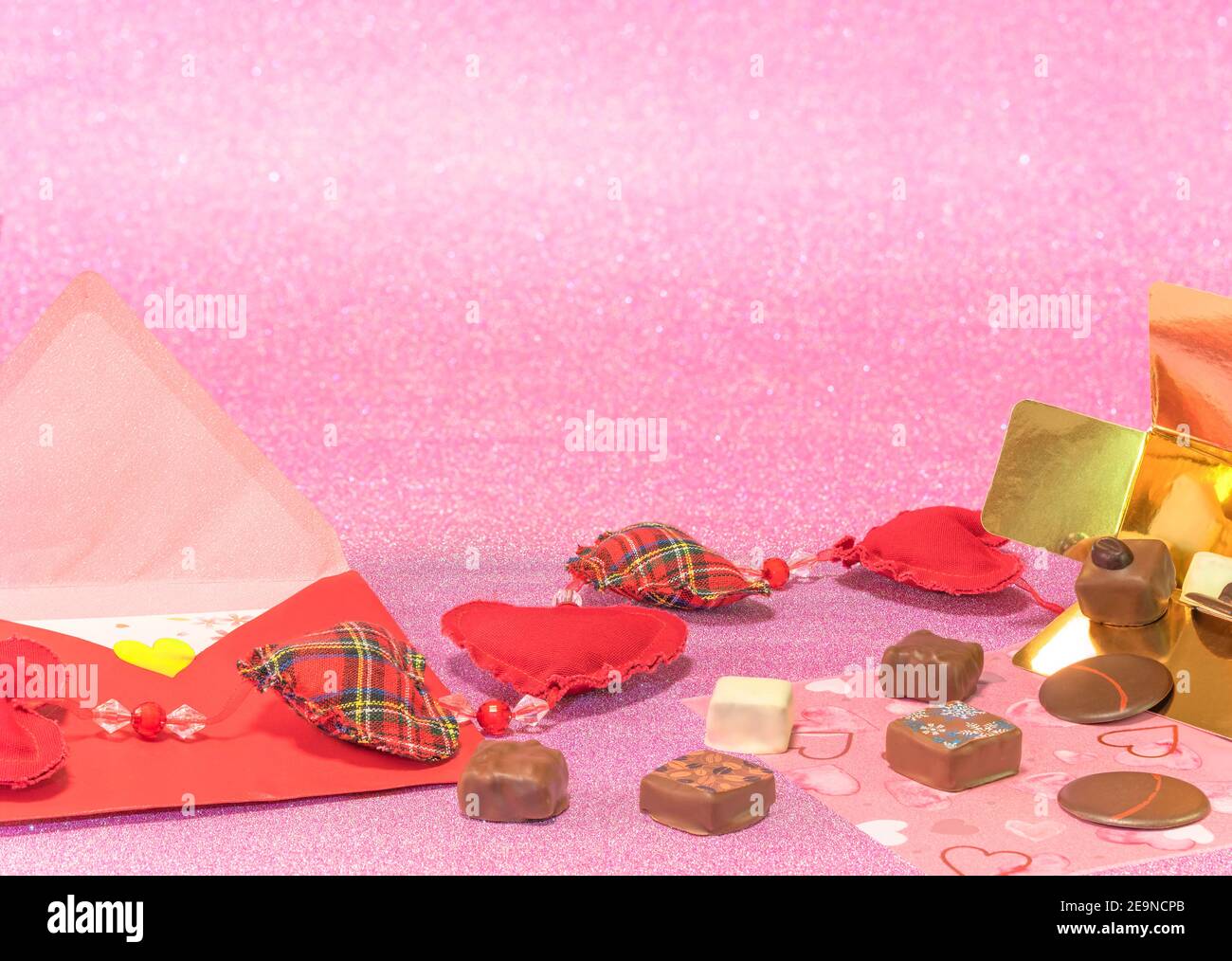 Grußkarte mit Schokoladen-Box und einem Liebesbrief mit einer Schrott-Wärme-Girlande auf einem glitzernden rosa Hintergrund feiern Valentinstag oder weißen Tag. Stockfoto