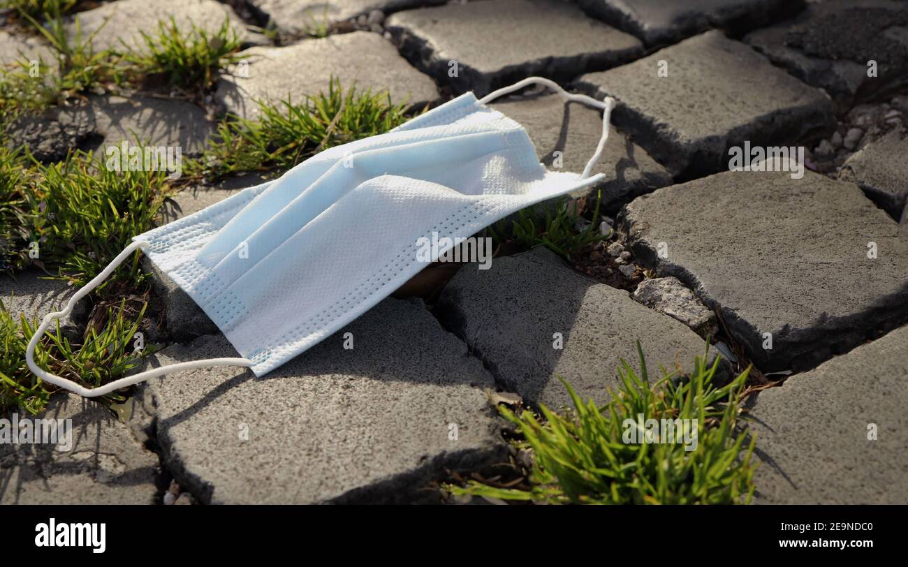 Eine Nahaufnahme Medizinische Schutzmaske auf den Boden geworfen. Abfalleimer medizinische Gesichtsmaske auf der Straße. Stockfoto