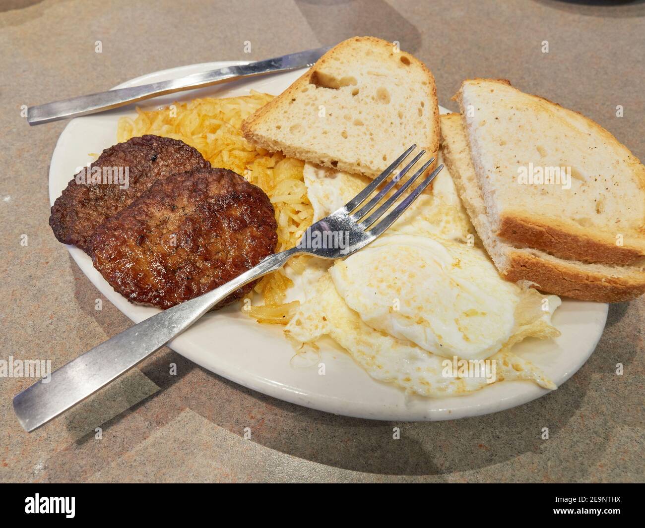 Amerikanisches Frühstück mit Eiern, Kartoffelrösti, Bratwurst und Toast in einem Restaurant. Stockfoto