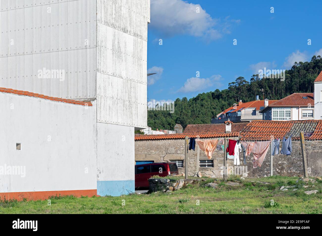 Europa, Spanien, Galicien, Porto do Son, traditionelle Wohnhäuser im Schatten eines großen Industriegebäudes Stockfoto