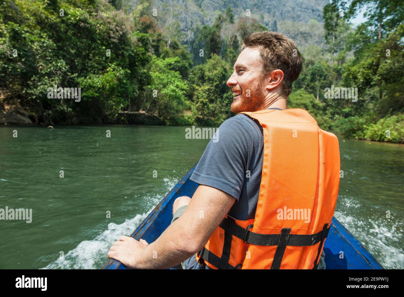 Junger Mann genießt eine Fahrt auf einem langen Boot In Laos Stockfoto