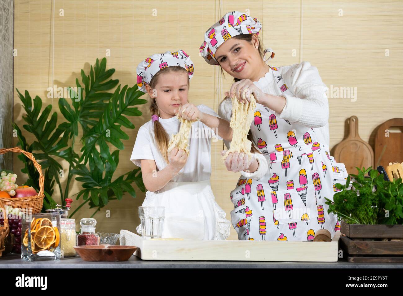 Die Mädchen, also Mutter und fünfjährige Tochter, ziehen den Kuchen in die Hände, um ihn abzureißen. Viel Spaß. Die Freude der gemeinsamen Momente von Mutter und Tochter während der Arbeit in der Küche. Stockfoto