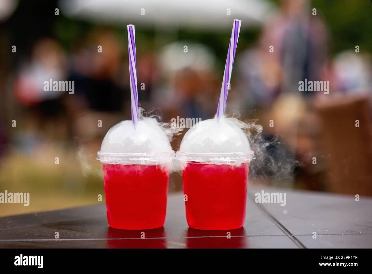 Bei einem Street Food Festival werden bunte Cocktails in Einweggläsern mit Strohhalmen auf der Theke ausgestellt, die von künstlichem Eis im Inneren rauchen. Wein Stockfoto