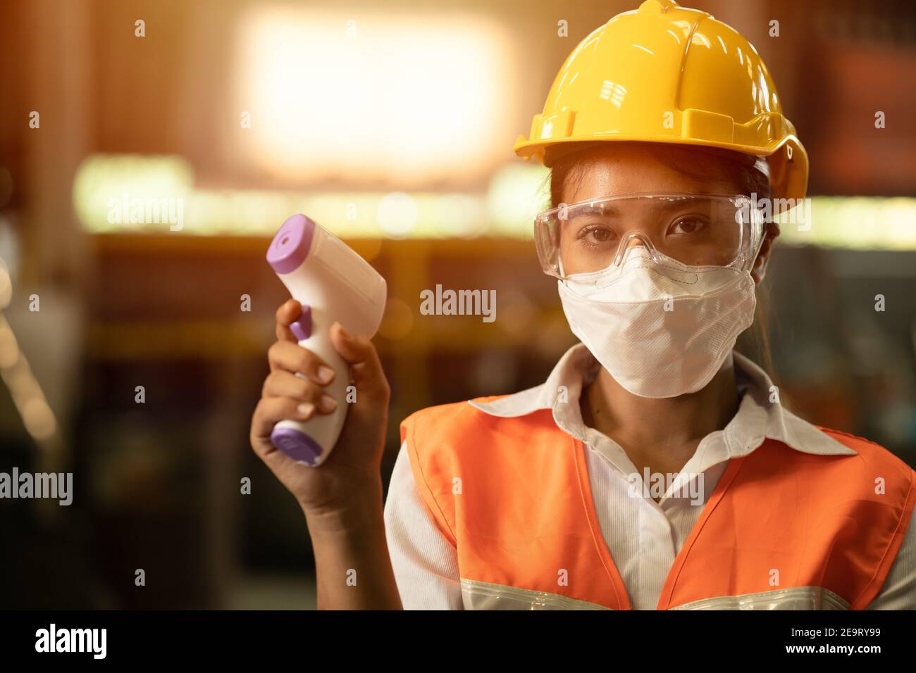 Industriearbeiterinnen tragen Gesichtsmaske und überprüfen die Körpertemperatur während der Coronavirus (COVID-19) Pandemie. Stockfoto