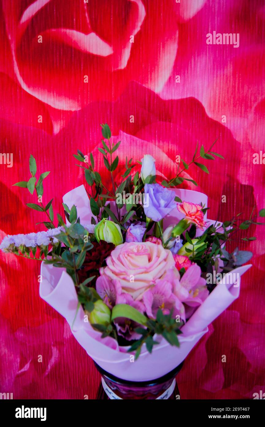 Ein zartes Blumenstrauß mit verschiedenen Blumen in einem hellrosa Wrapper steht in einer häuslichen Umgebung gegen eine bunte rosafarbene Wand. Vertikales Foto. Stockfoto