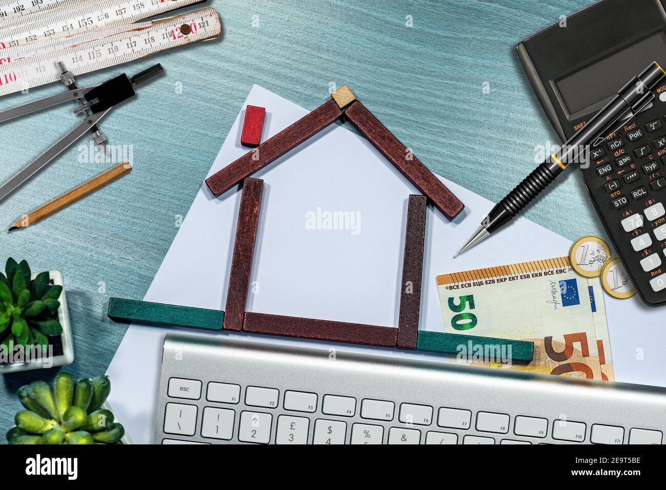 Kleines Holzhaus aus Spielzeugblöcken auf dem Schreibtisch, mit Euro-Währung, Taschenrechner, Klapplineal. Immobilieninvestments Konzept. Stockfoto