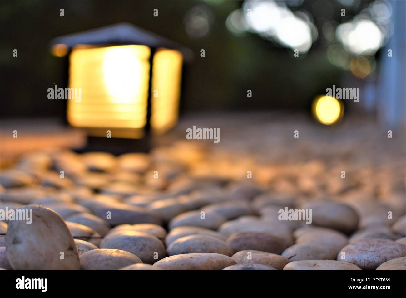 Weiße Kieselsteine mit einer beleuchteten Gartenlampe im Hintergrund Stockfoto