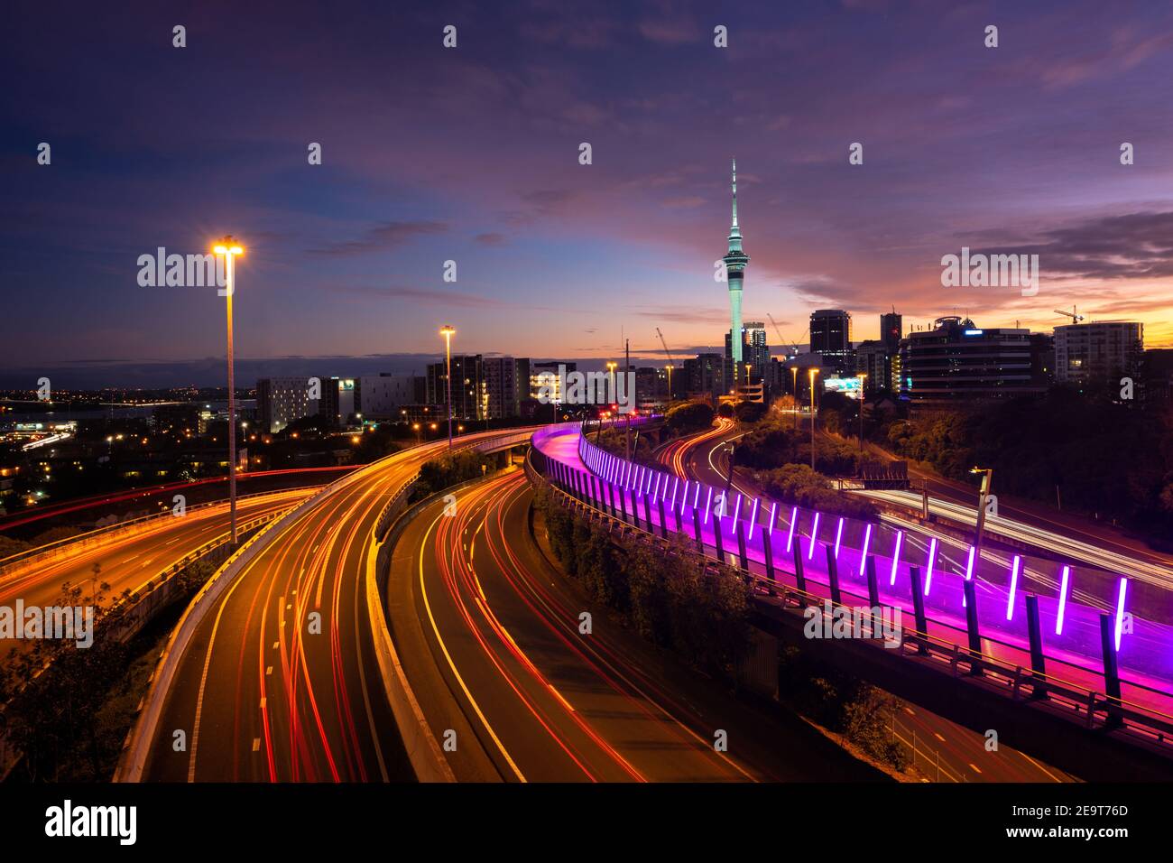 Blick auf die Skyline von Auckland, den Sky Tower und die Autobahn mit Autowegen bei Sonnenaufgang. Stockfoto