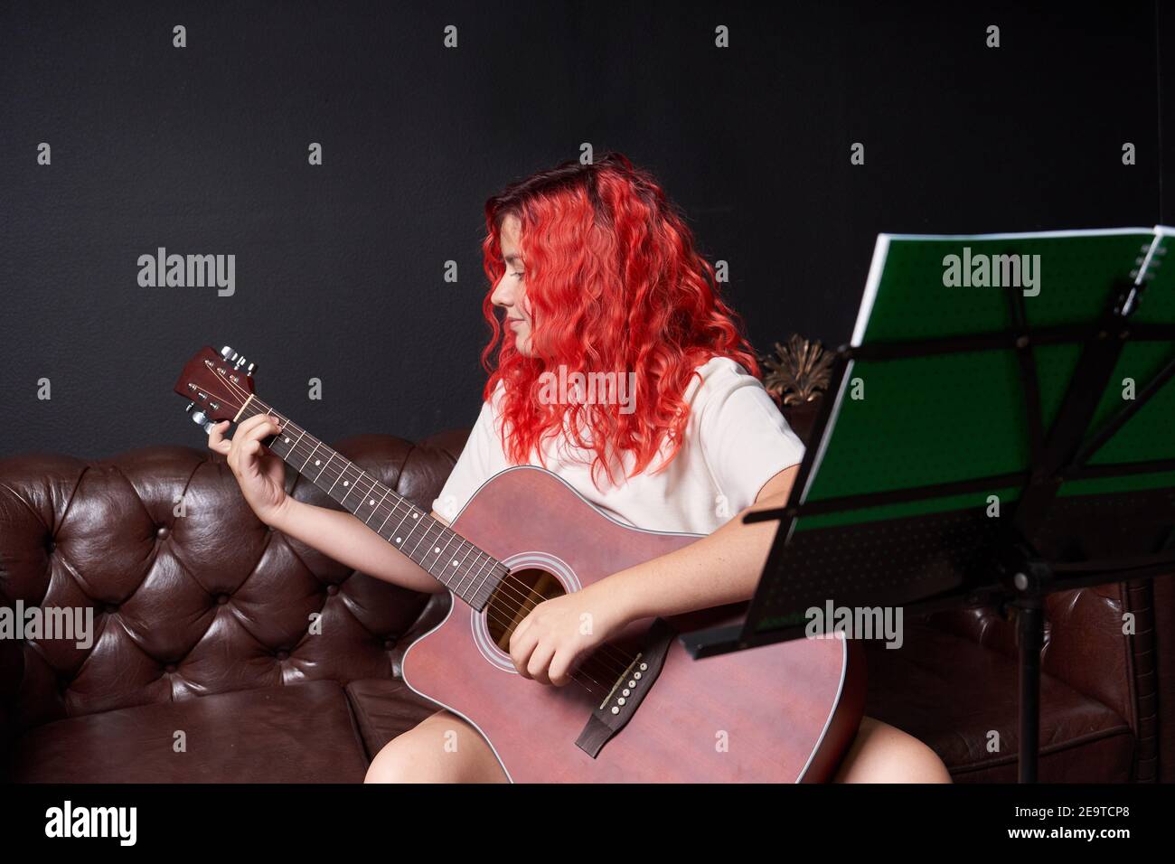 Teenager-Mädchen mit roten Haaren lächelnd lernt, die zu spielen Akustische Gitarre Stockfoto