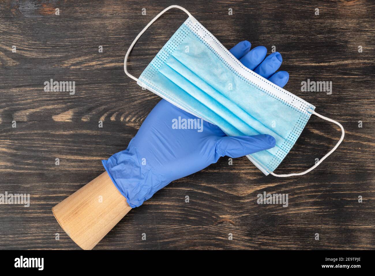 Schaufensterpuppe Hand trägt einen Einweghandschuh und hält eine medizinische Maske. Während der Quarantäne von covid19. Stockfoto