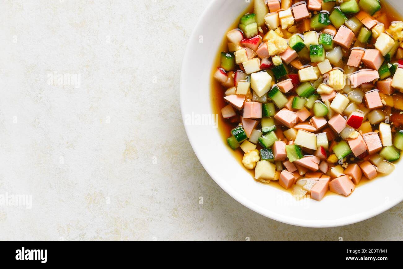 Nahaufnahme der kalten russischen Suppe Okroshka mit Wurst, Gemüse und Kvass auf hellem Stein Hintergrund mit freien Text Raum. Draufsicht, flach liegend Stockfoto